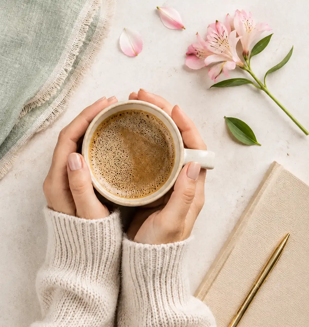 Hands wrapped around a cup of coffee, surrounded by pink flower petals